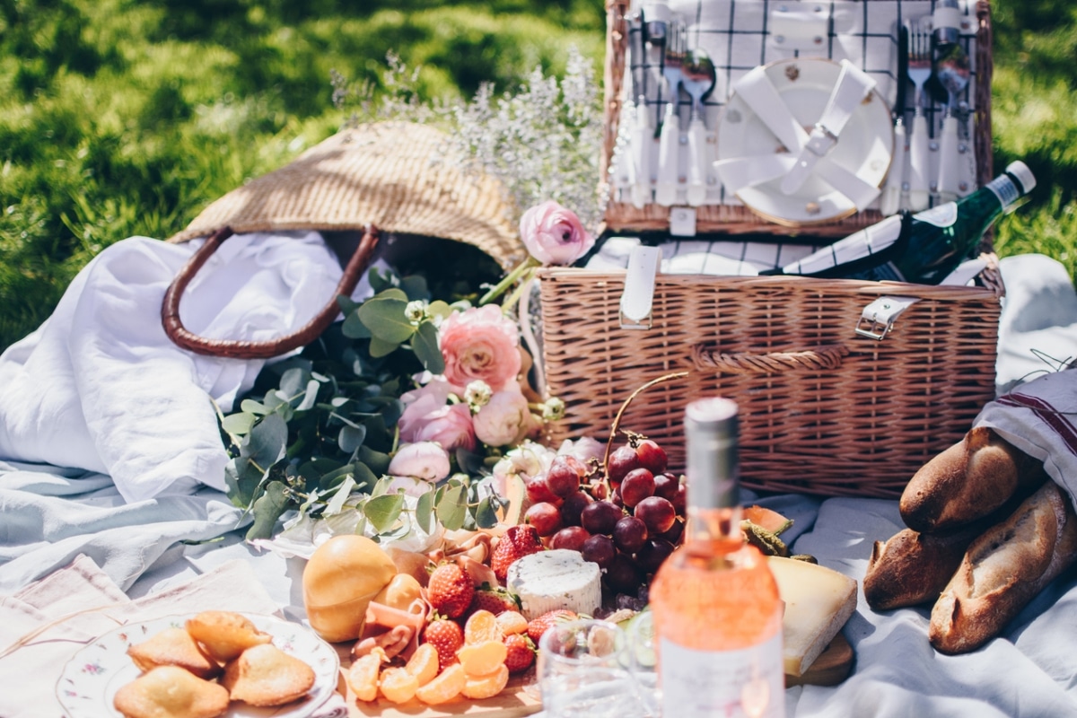 A picnic setup for Valentine's Day, with flowers, a charcuterie board, a bottle of wine, and fresh flowers.