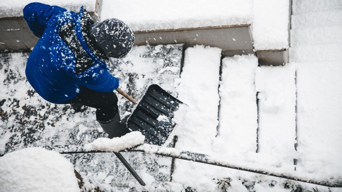 A man clearing layers of snow off of his home staircase during winter.